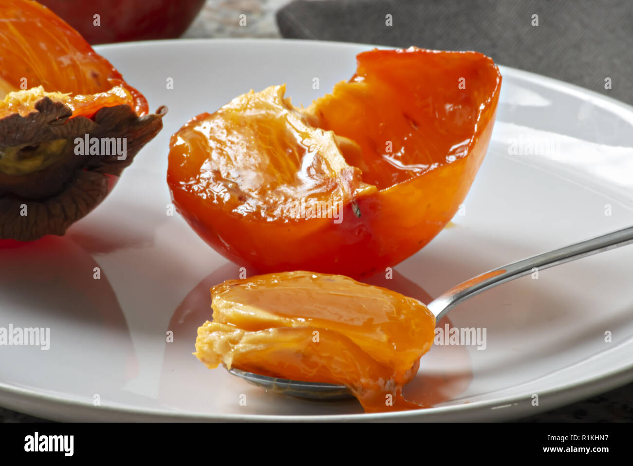 khaki fruit in the plate cut in half and full teaspoon close-up Stock Photo