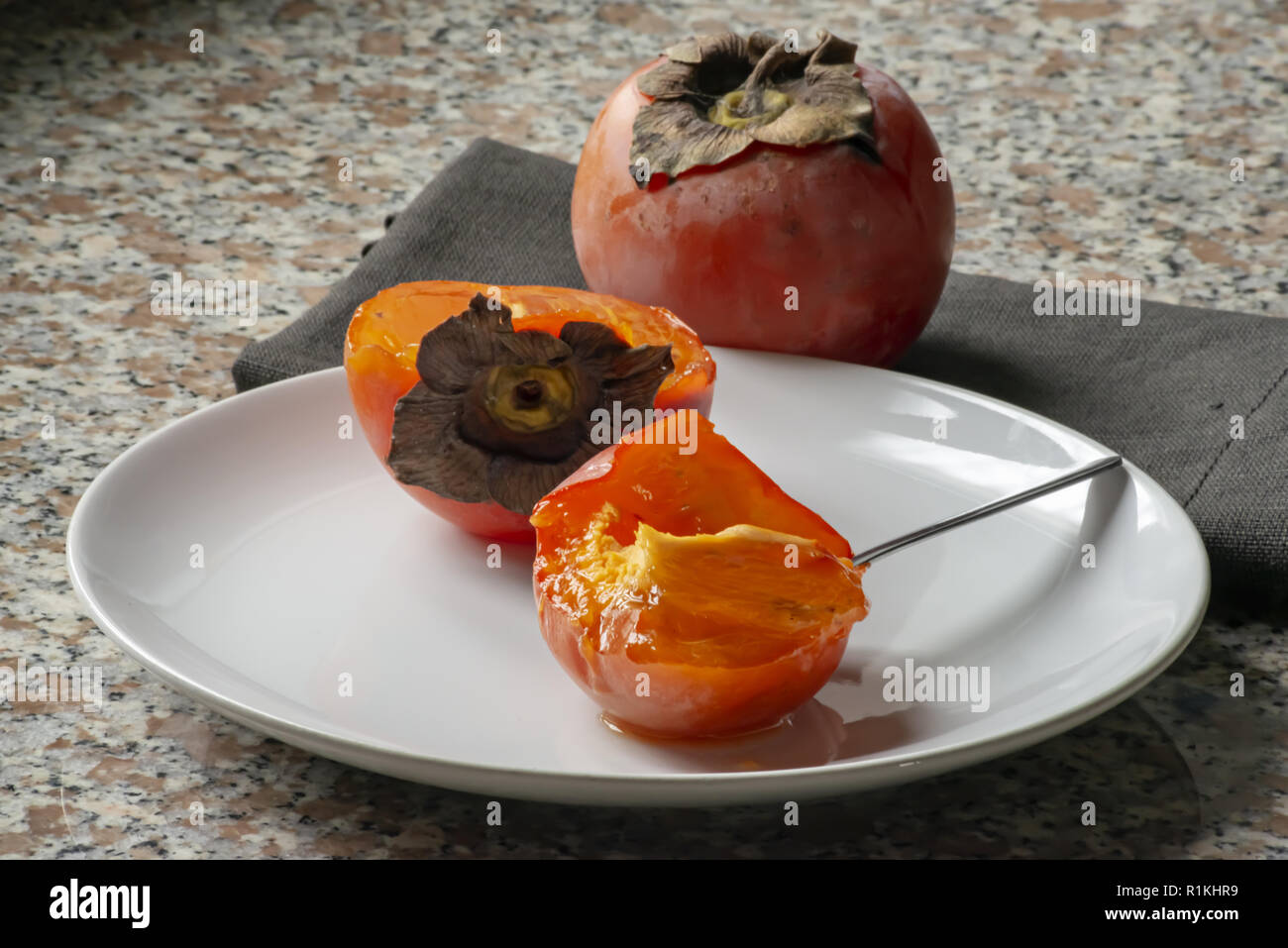 kaki fruit in the plate cut in half and full front spoon Stock Photo