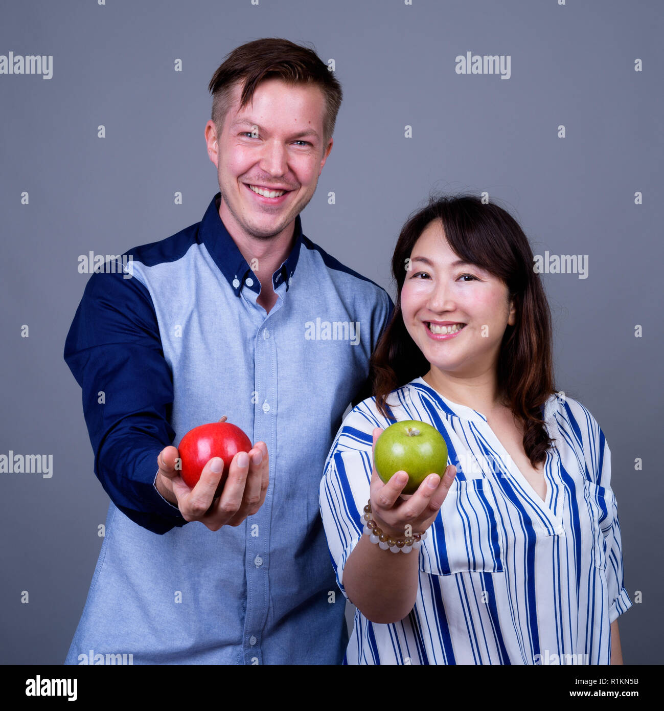 Multi ethnic diverse couple in studio holding green and red apple fruit Stock Photo