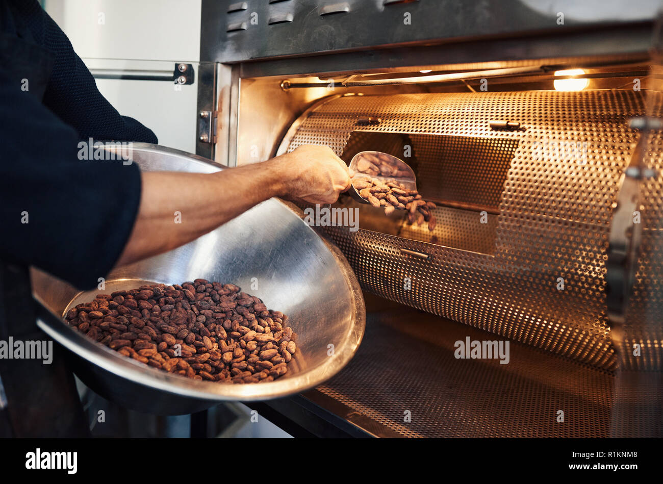 Chocolate making factory worker putting cocoa beans into a roaster