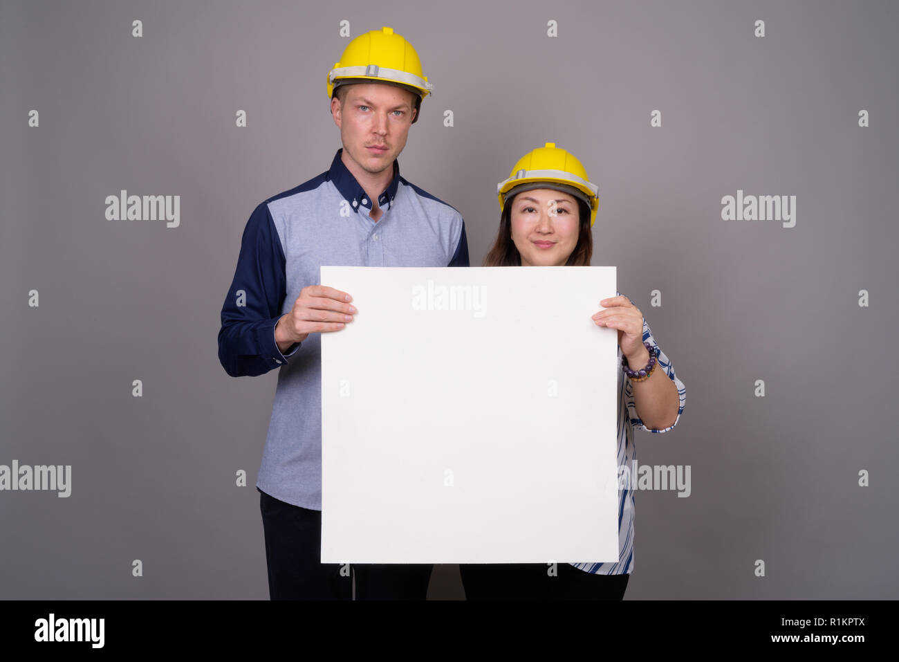 Businessman and mature Asian businesswoman wearing hardhat Stock Photo