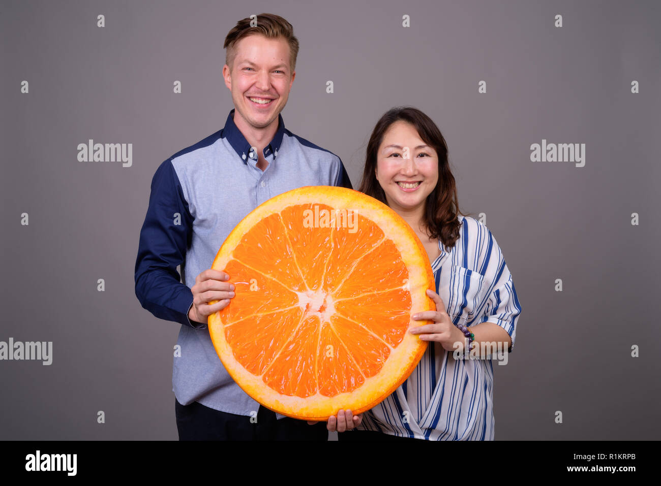 Businessman and mature Asian businesswoman holding big orange slice Stock Photo