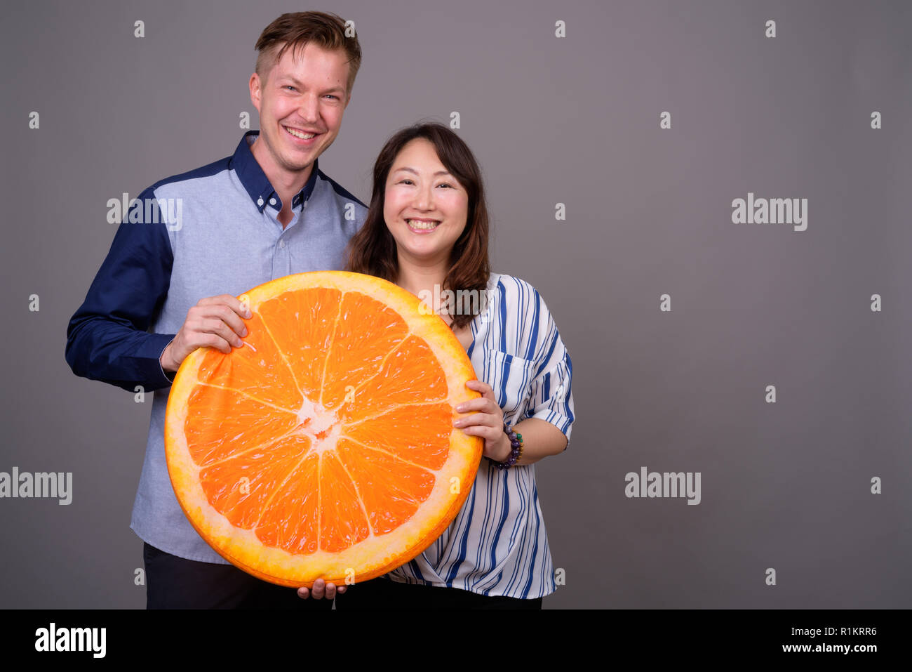 Businessman and mature Asian businesswoman holding big orange slice Stock Photo