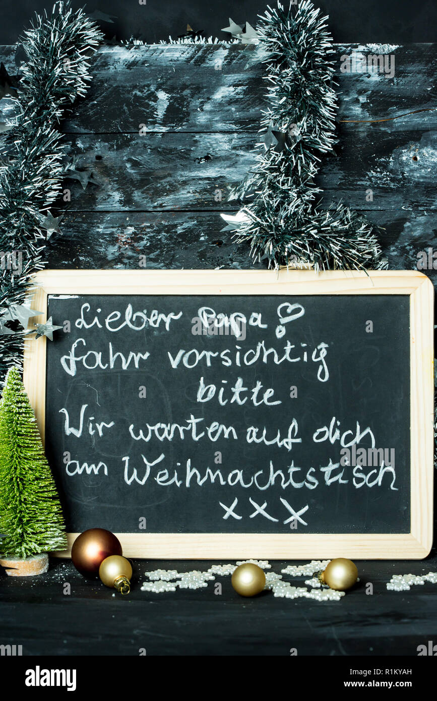 on a Christmas background a blackboard with a message in german language from child to father: Drive carefully, we are waiting at Christmas table for Stock Photo