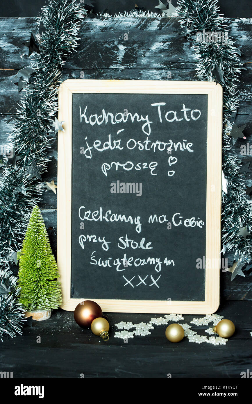 on a Christmas background a blackboard with a message in polish language from child to father: Drive carefully, we are waiting at Christmas table for Stock Photo