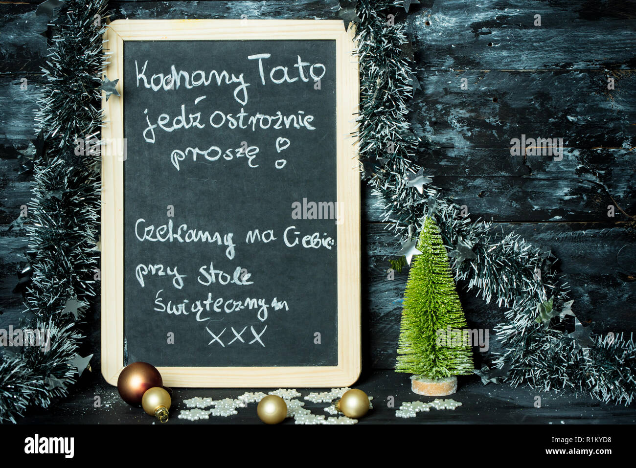 on a Christmas background a blackboard with a message in polish language from child to father: Drive carefully, we are waiting at Christmas table for Stock Photo