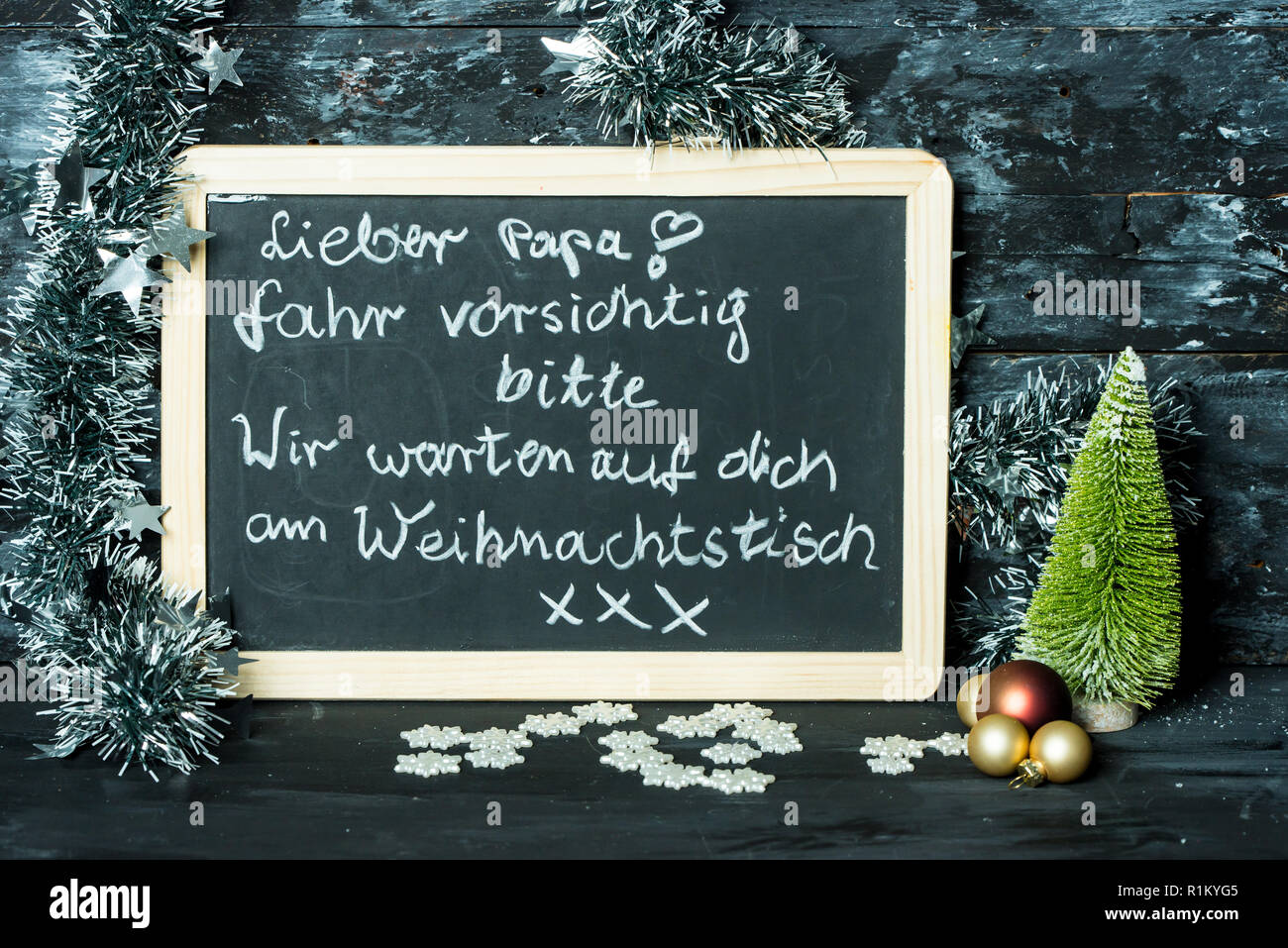 on a Christmas background a blackboard with a message in german language from child to father: Drive carefully, we are waiting at Christmas table for Stock Photo