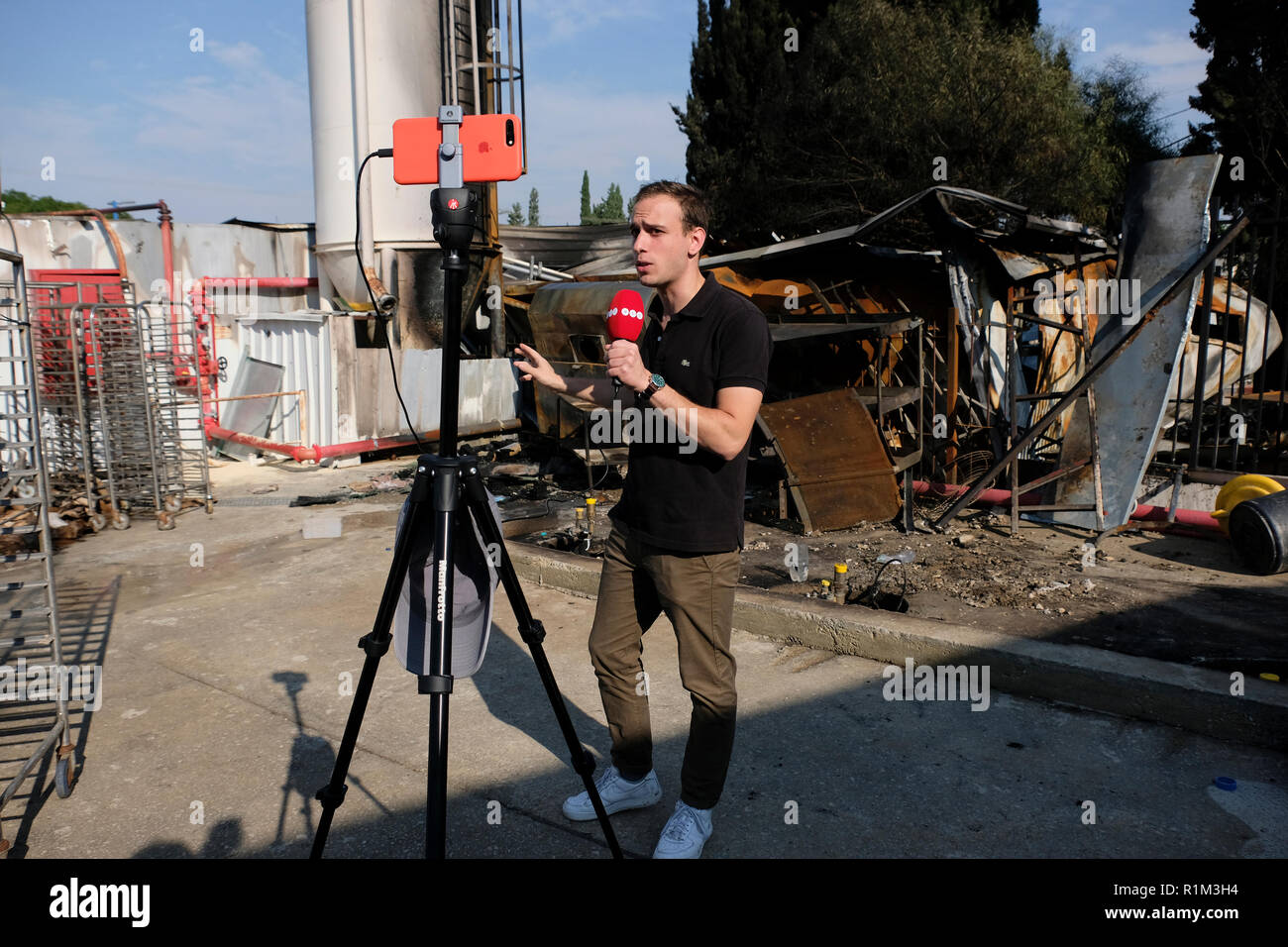 Turai Barnabas a reporter of ATV Hungarian private TV channel speaking into  a microphone in front of a smartphone at the site that was struck by a  rocket fired from Gaza strip