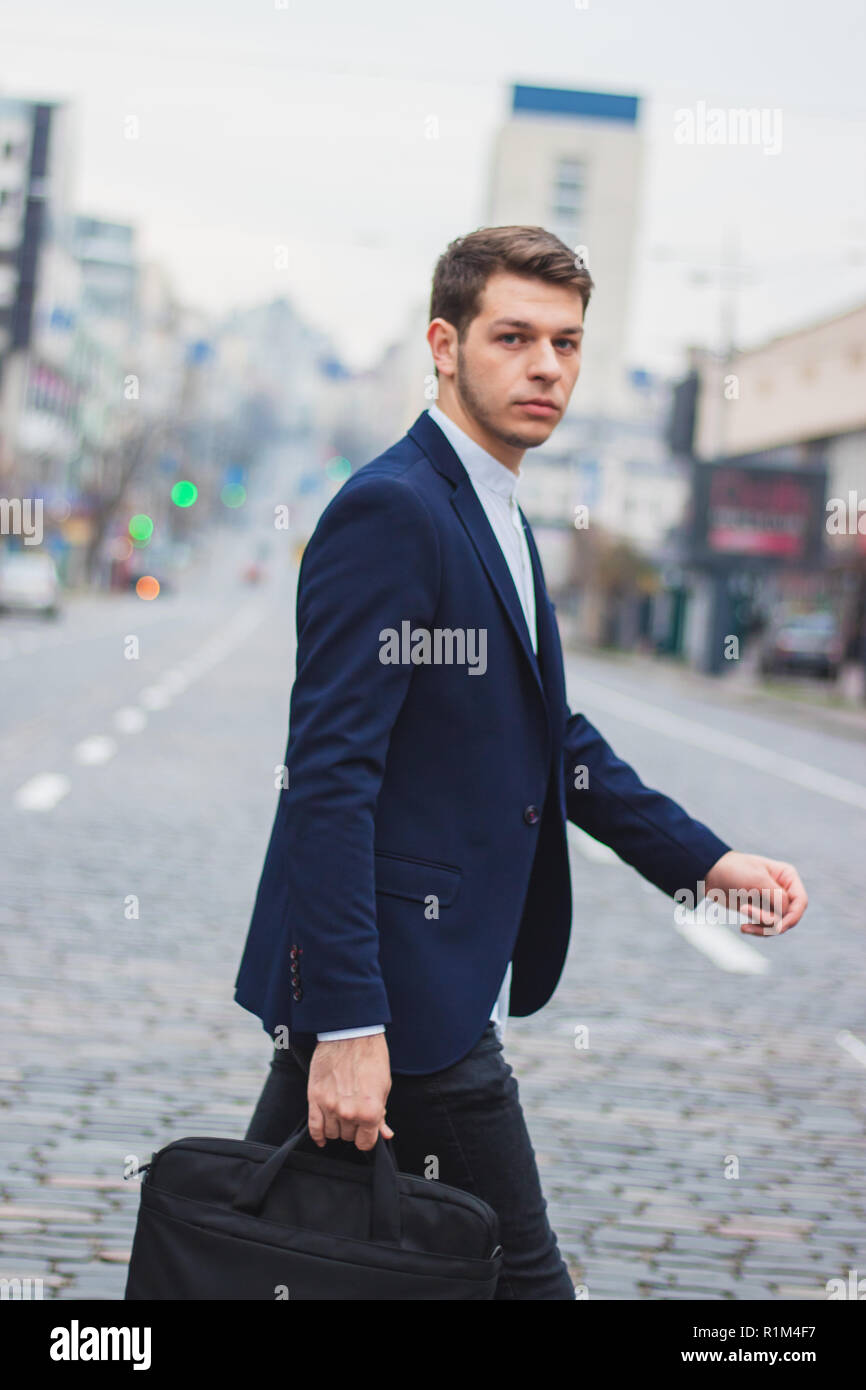 Business style. A young businessman is crossing the road. In his hand holds a briefcase. Go to meet. Go to work. Stock Photo