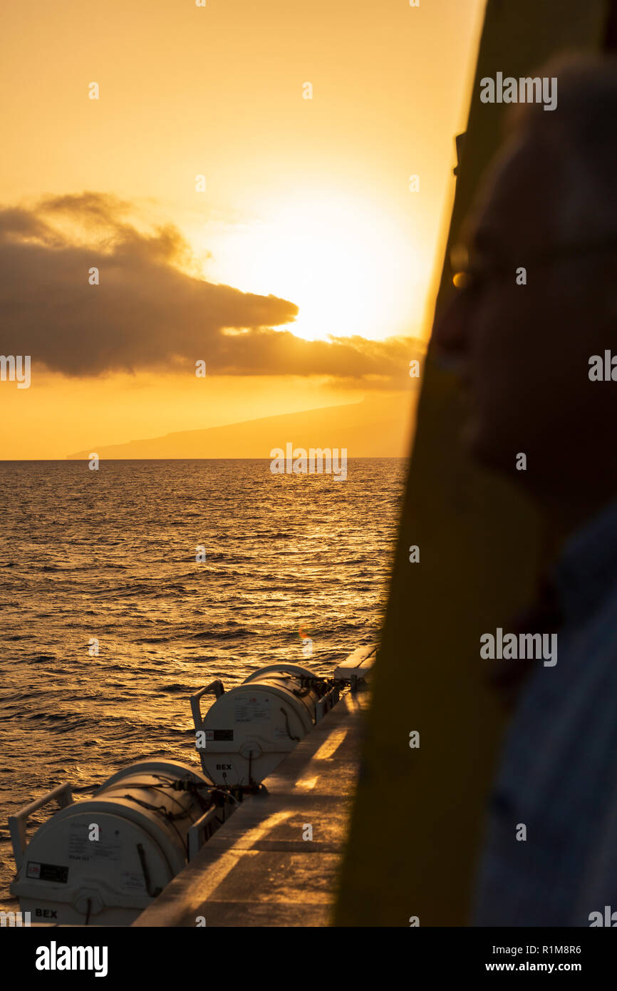Sunset over the island of La Gomera seen from the deck of an inter island ferry with lifeboat pods in foreground, Tenerife, Canary Islands, Spain Stock Photo