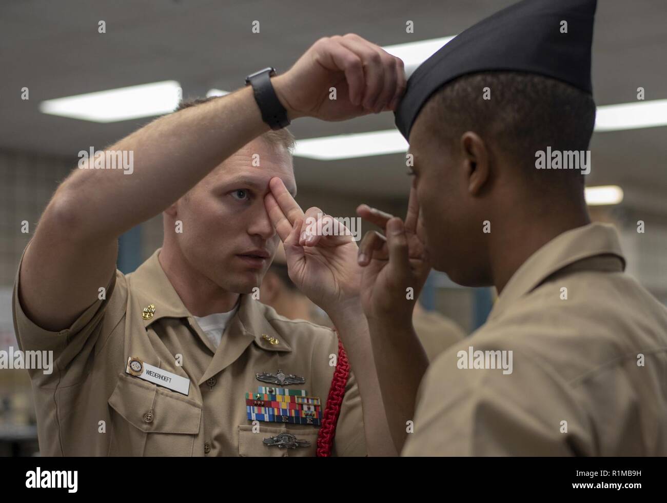 GREAT LAKES, Ill. (Oct. 23, 2018) Chief Gunner's Mate Jeremiah Wiederhoeft, a recruit division commander, assists a recruit from his division in the proper fitting and wear of the garrison cover inside the Uniform Issue building at Recruit Training Command. More than 30,000 recruits graduate annually from the Navy's only boot camp. Stock Photo