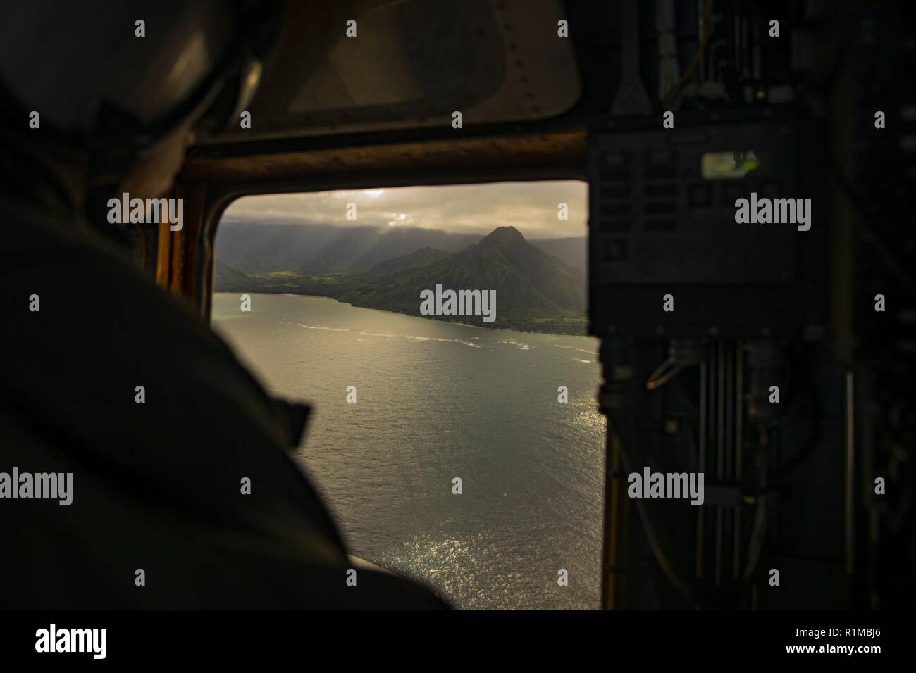 U.S. Marine Corps Lance Cpl. Tyler Wetmore, an aerial observer with Marine Heavy Helicopter Squadron 463, Marine Aircraft Group 24, observes out the side hatch of a CH-53E Super Stallion during flight operations over the island of Oahu, Oct. 22, 2018.  The flight was conducted to produce readiness within the squadron. Stock Photo