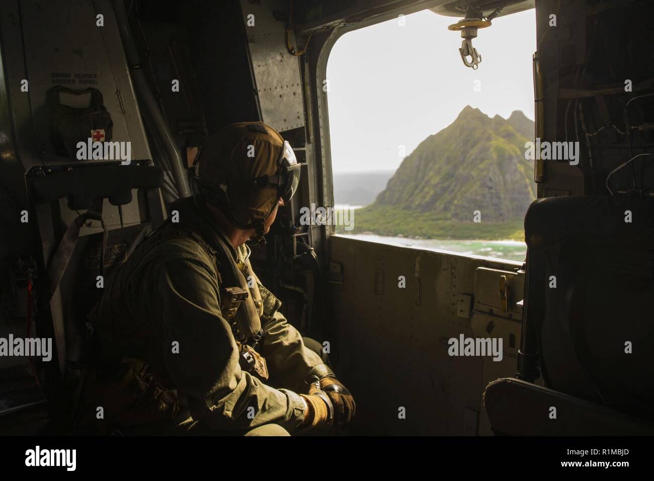 U.S. Marine Corps Gunnery Sgt. Todd Bauer, a crew chief with Marine Heavy Helicopter Squadron 463, Marine Aircraft Group 24, observes out the side door of a CH-53E Super Stallion during flight operations over the island of Oahu, Oct. 22, 2018. The flight was conducted to produce readiness within the squadron. Stock Photo