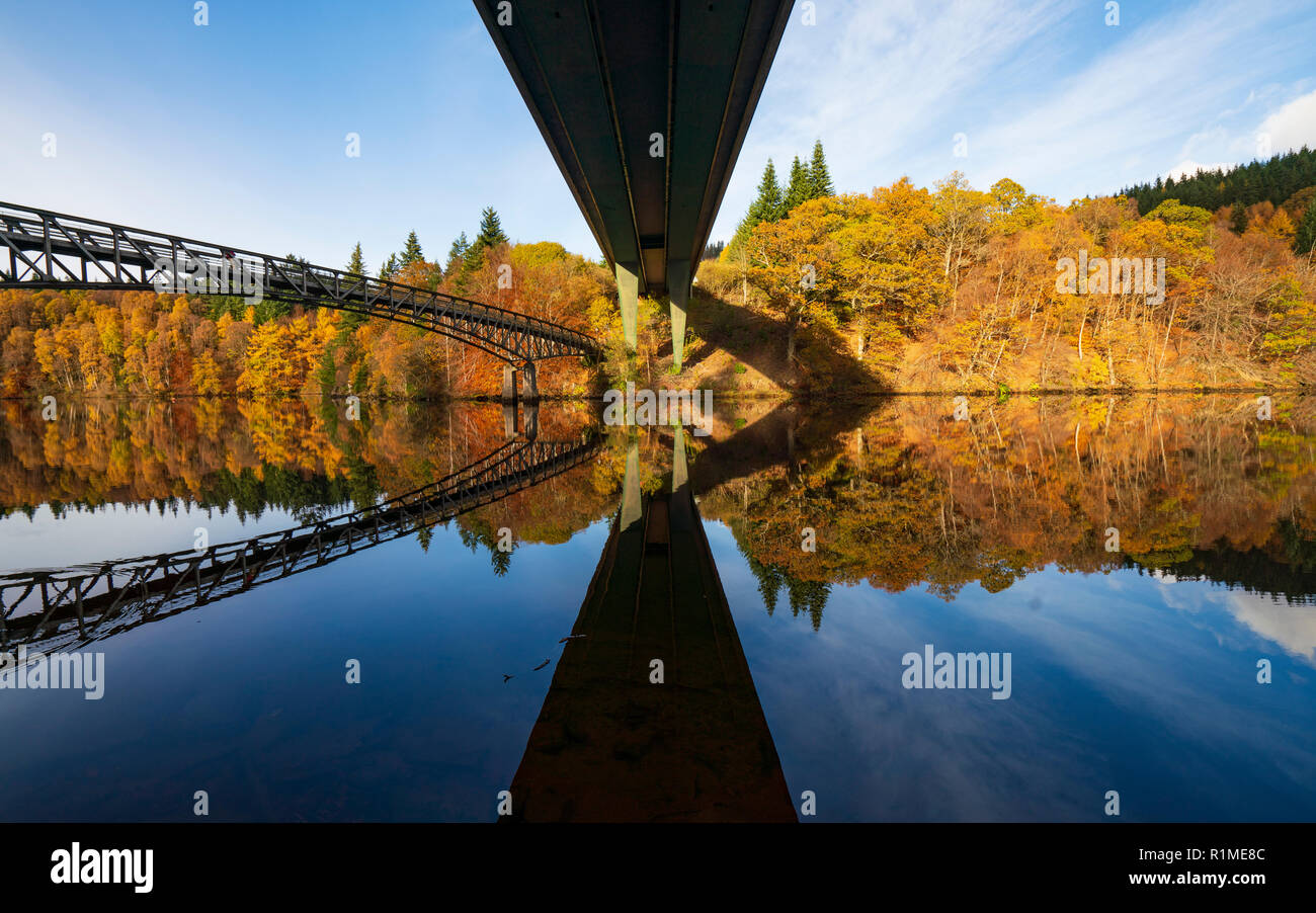 Spectacular late autumn tree colours and twin bridges are reflected in the waters of Loch Faskally in Pitlochry, Perthshire, Scotland, UK. Stock Photo