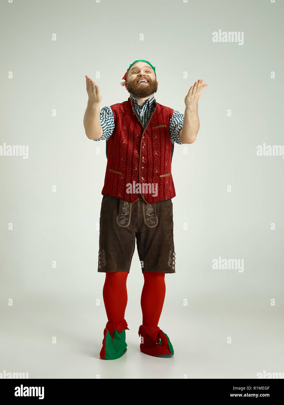 The happy smiling friendly man dressed like a funny gnome or elf posing on an isolated gray studio background. The winter, holiday, christmas concept Stock Photo