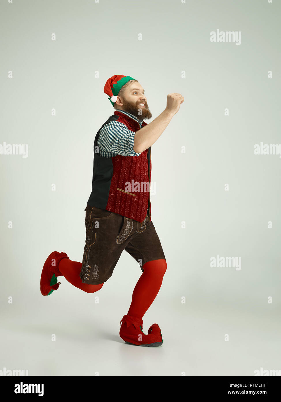 The happy smiling friendly man dressed like a funny gnome or elf running on an isolated gray studio background. The winter, holiday, christmas concept Stock Photo