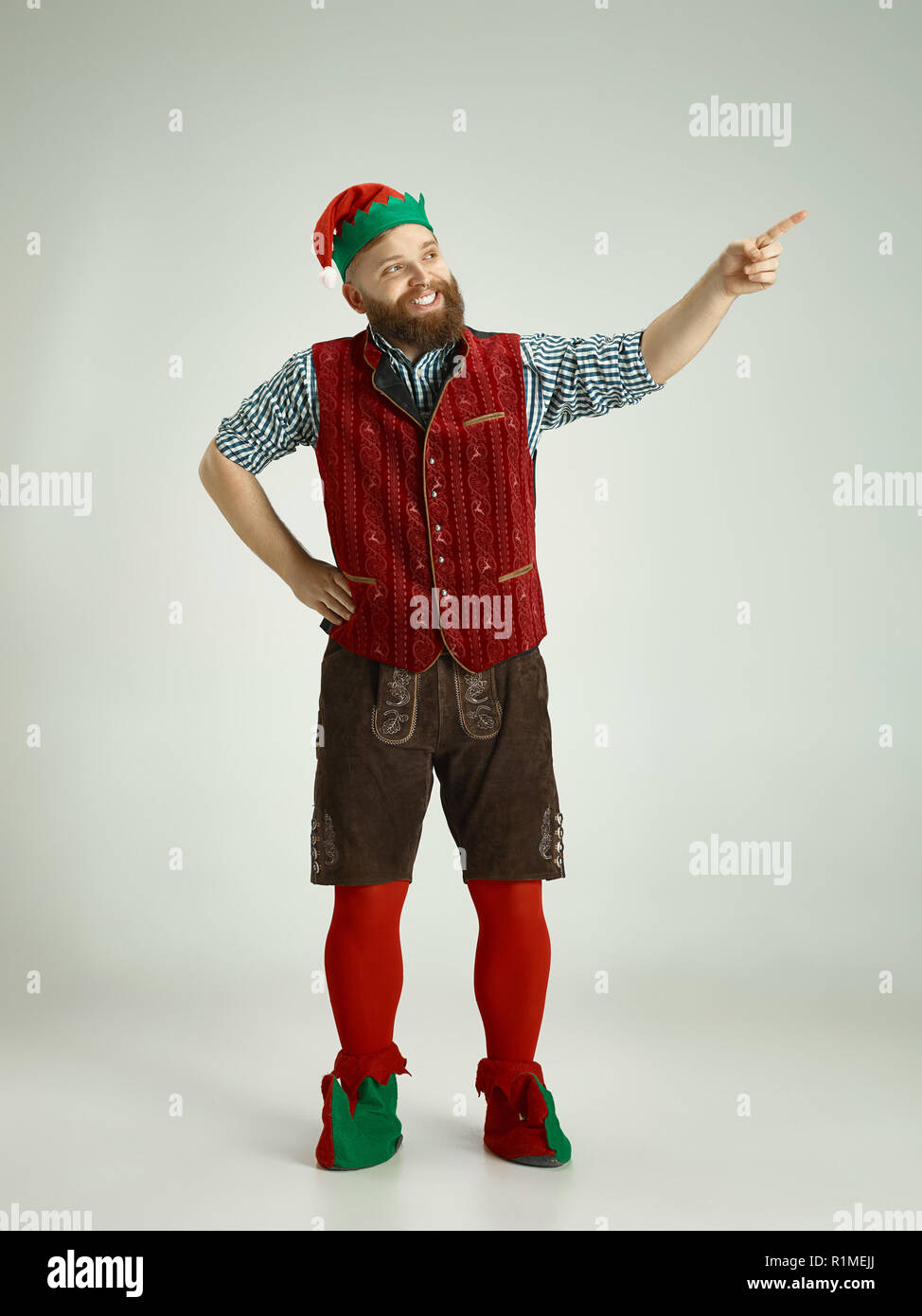 The happy smiling friendly man dressed like a funny gnome or elf posing on an isolated gray studio background. The winter, holiday, christmas concept Stock Photo