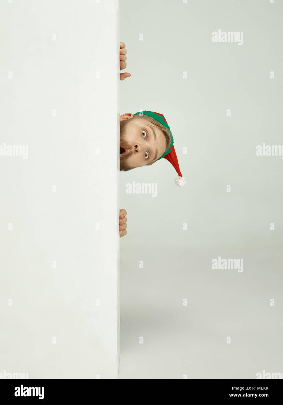 The happy smiling friendly man dressed like a funny gnome or elf posing on an isolated gray studio background. The winter, holiday, christmas concept Stock Photo