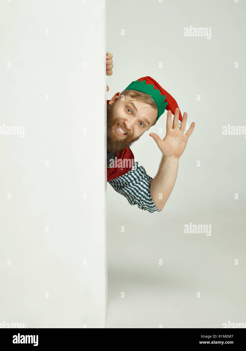 The happy smiling friendly man dressed like a funny gnome or elf posing on an isolated gray studio background. The winter, holiday, christmas concept Stock Photo