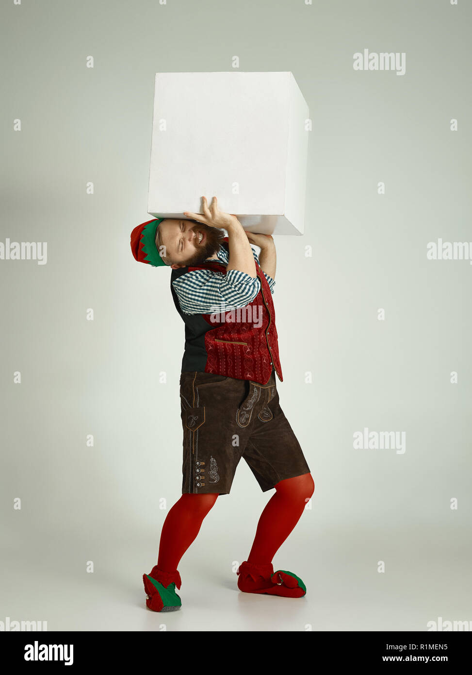 The happy smiling friendly man dressed like a funny gnome or elf posing on an isolated gray studio background. The winter, holiday, christmas concept Stock Photo