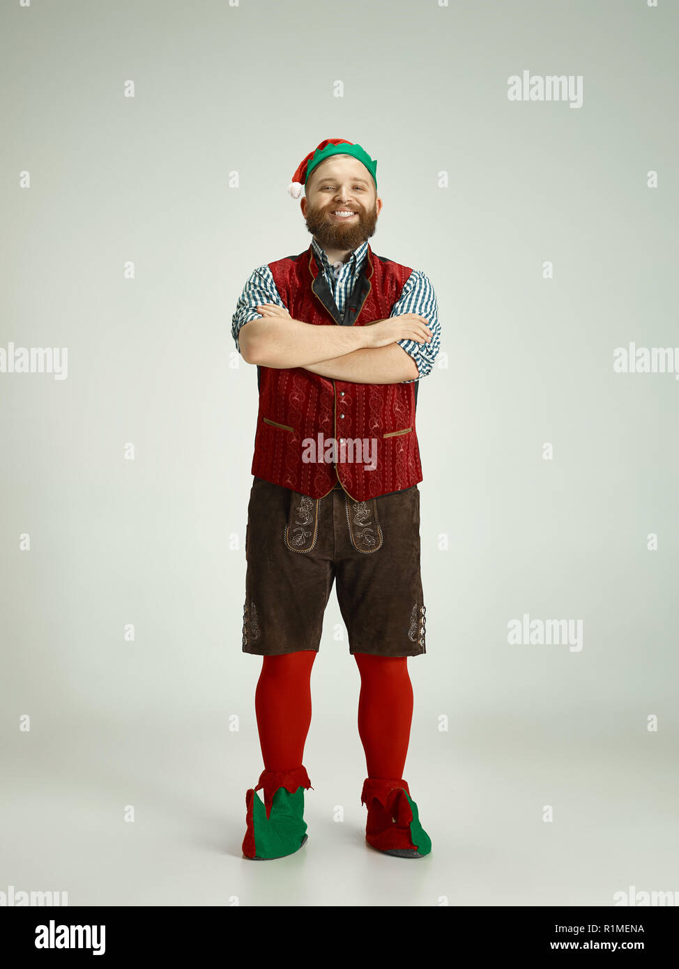 The happy smiling friendly man dressed like a funny gnome or elf posing on an isolated gray studio background. The winter, holiday, christmas concept Stock Photo