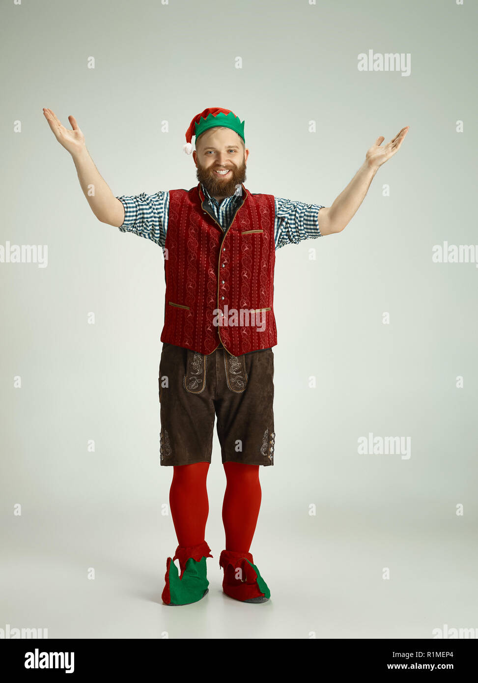 The happy smiling friendly man dressed like a funny gnome or elf posing on an isolated gray studio background. The winter, holiday, christmas concept Stock Photo