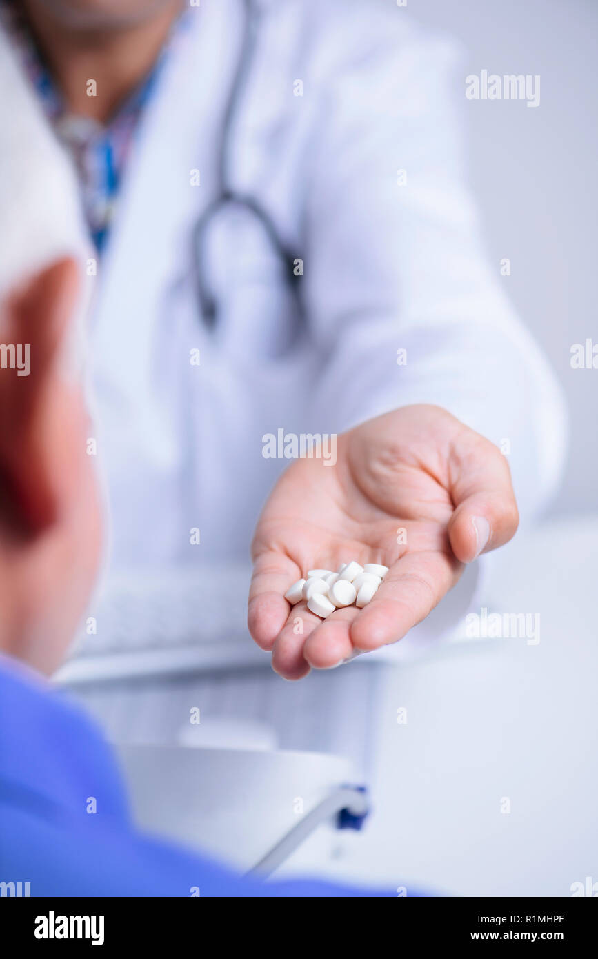 closeup of a caucasian doctor man, in a white coat, giving some pills to a senior caucasian patient man, sitting both at a doctors desk Stock Photo