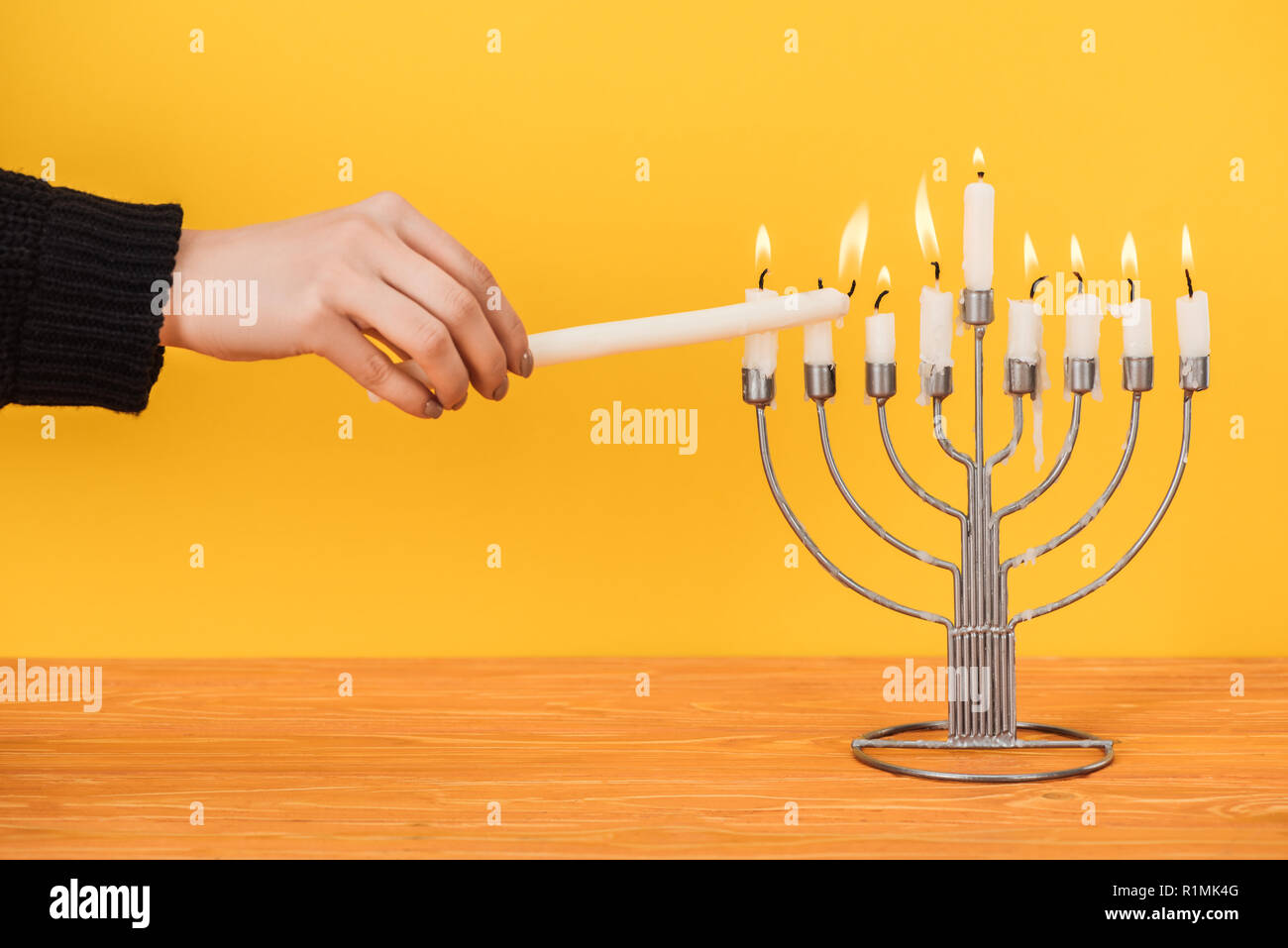 partial view of woman lighting candles on menorah isolated on yellow, hannukah holiday concept