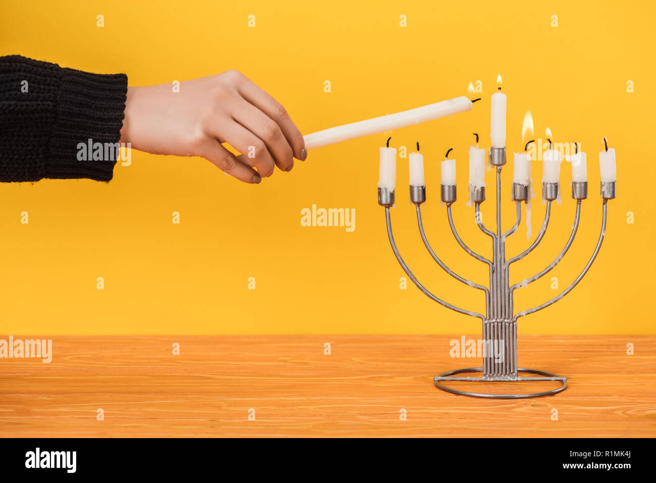 partial view of woman lighting candles on menorah isolated on yellow