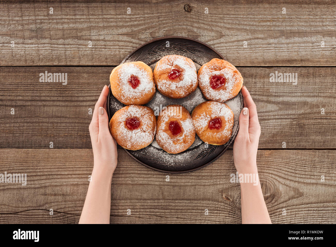 partial view of woman holding plate with sweet doughnuts hannukah traditional food on wooden surface, hannukah concept Stock Photo