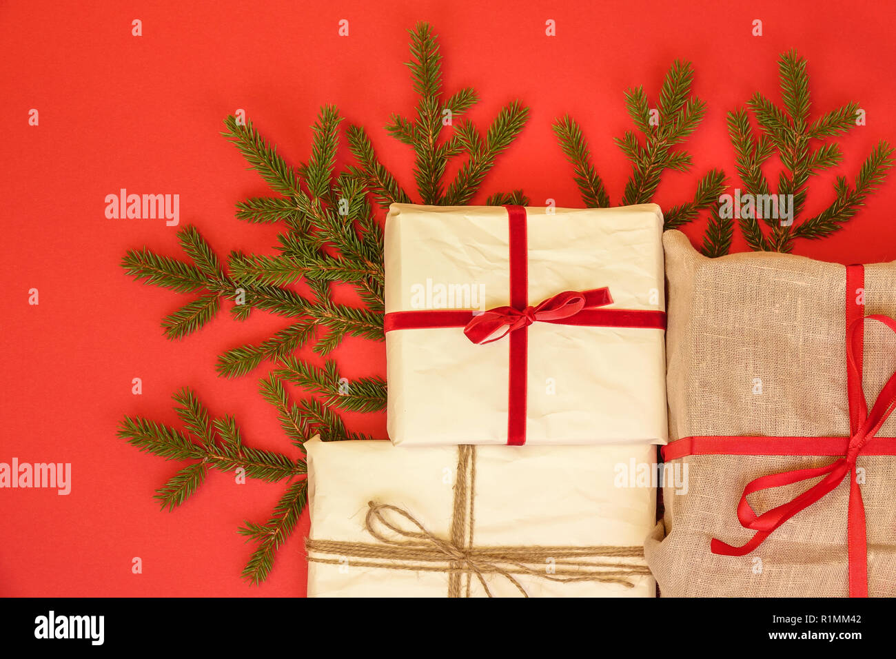 Fir branch / twig and christmas gift boxes on red background. Burlap and reused / recycled wrapping paper. Red ribbon and natural linen string. Stock Photo