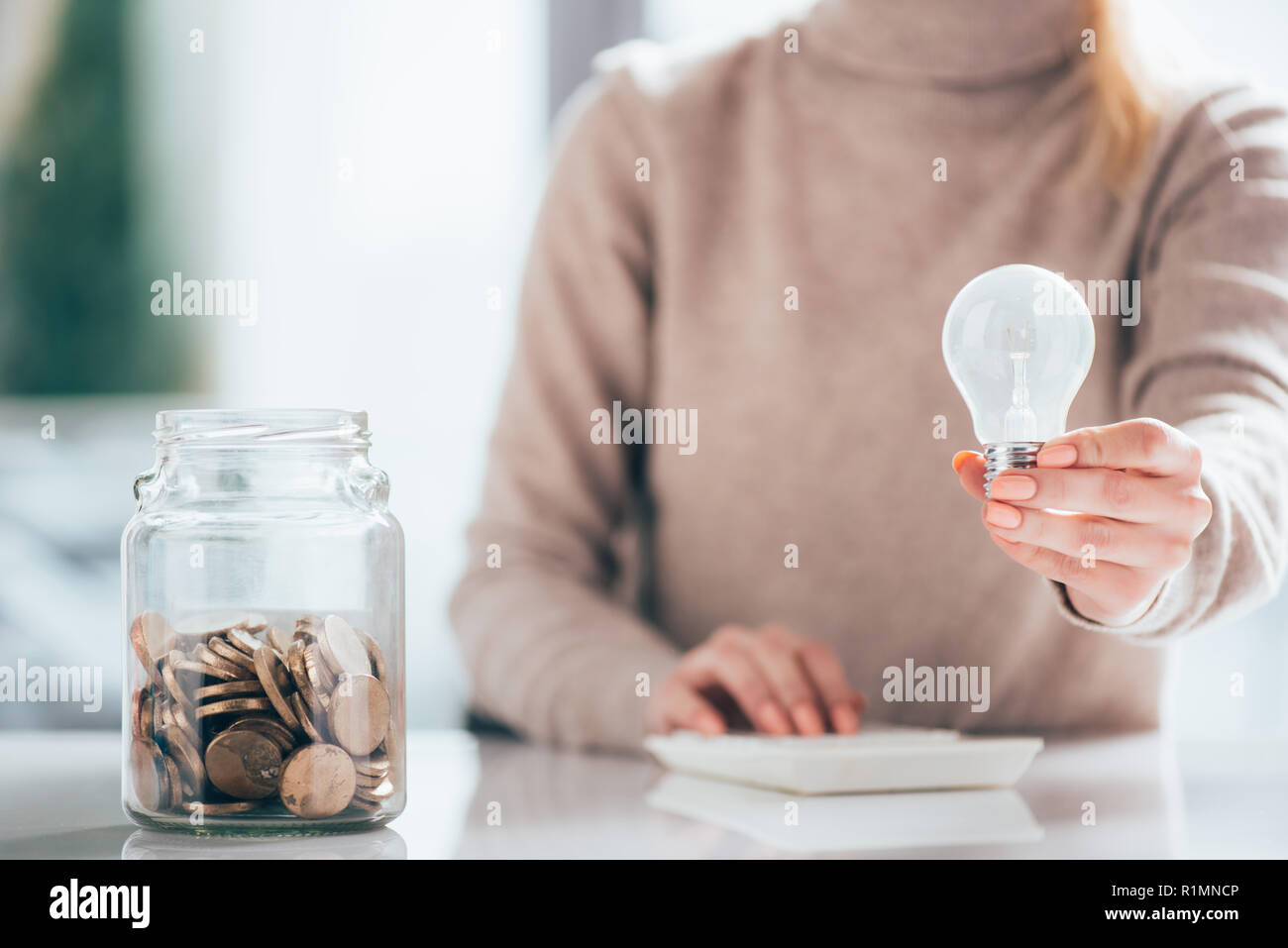 close-up view of glass jar with coins and woman holding light bulb Stock Photo