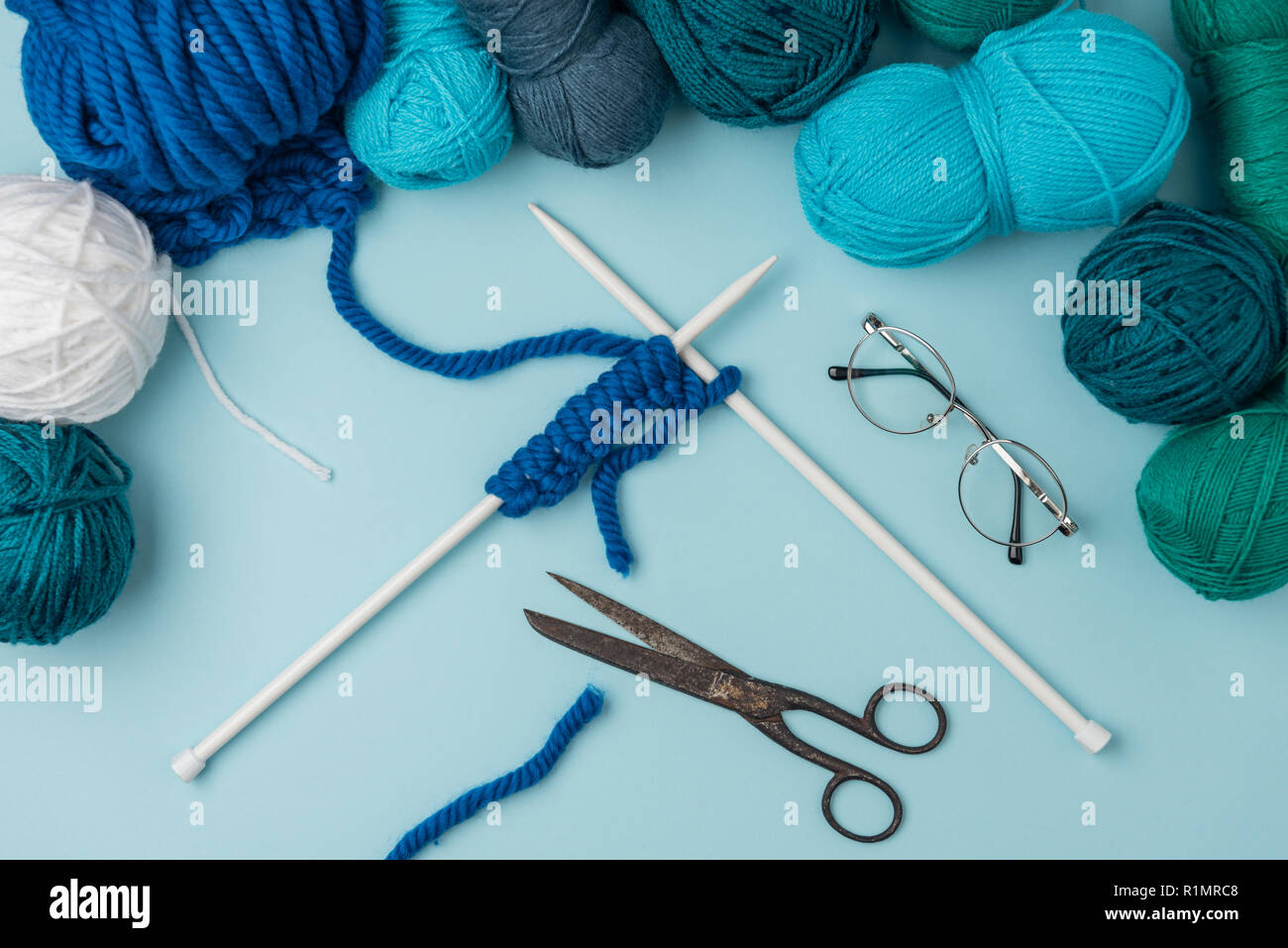 close up view of yarn, knitting needles, eyeglasses and scissors on blue backdrop Stock Photo