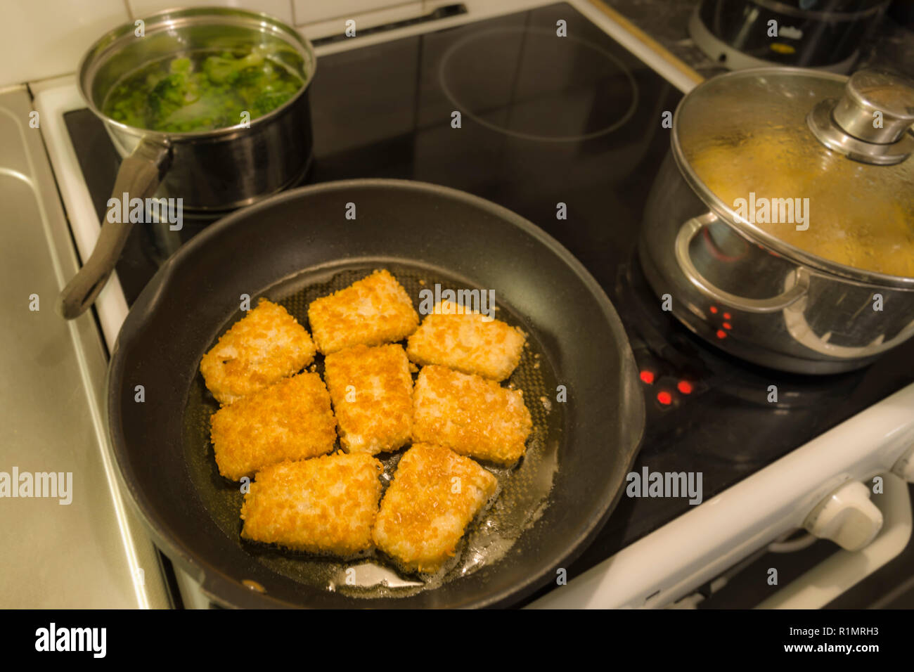 Breaded fish fillets sizzling in frying pan Stock Photo