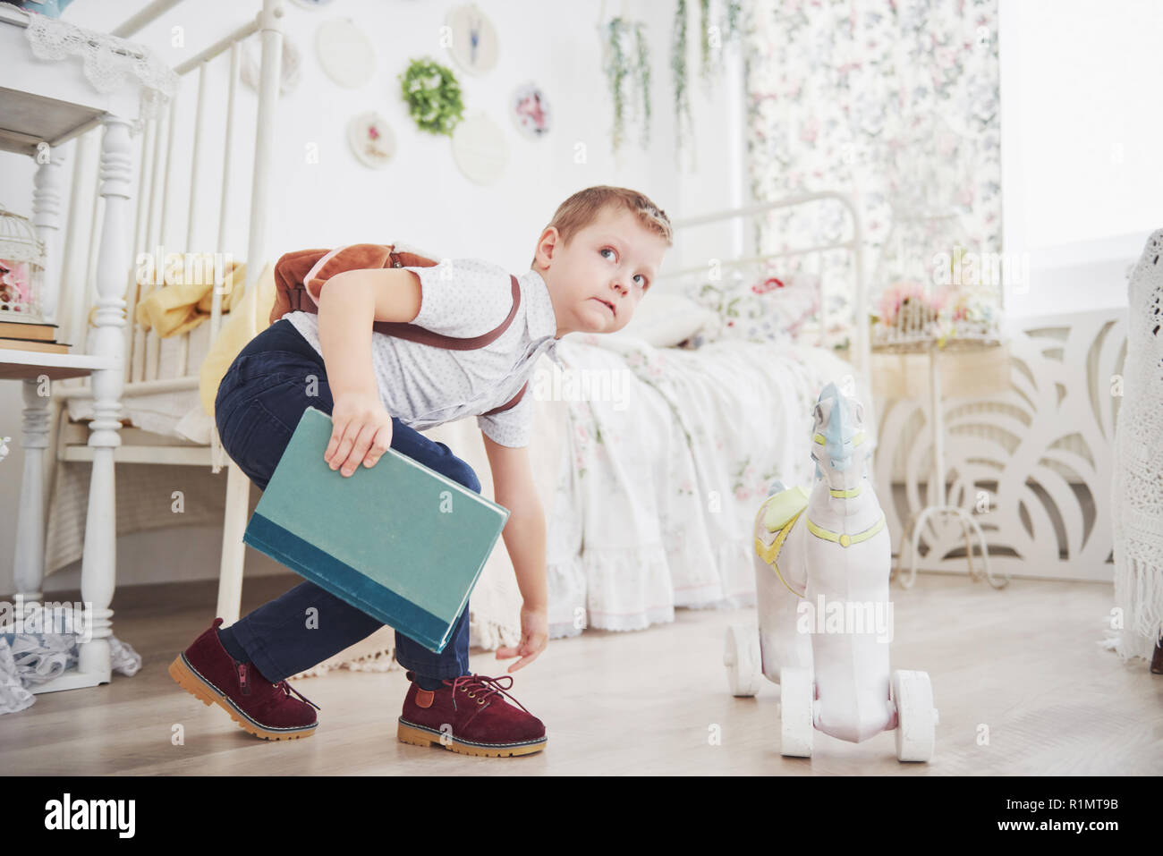 Cute little boy is going to school for the first time. Child with school bag and book. Kid makes a briefcase, child room on a background. Back to school Stock Photo