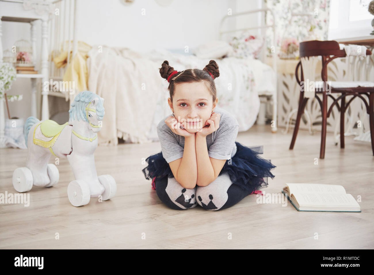 Cute little child girl reading a book in the bedroom. Kid with crown sitting on the bed near window Stock Photo