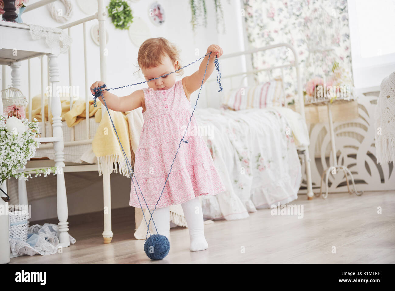 Childhood concept. Baby girl in cute dress play with colored thread. White vintage childroom Stock Photo