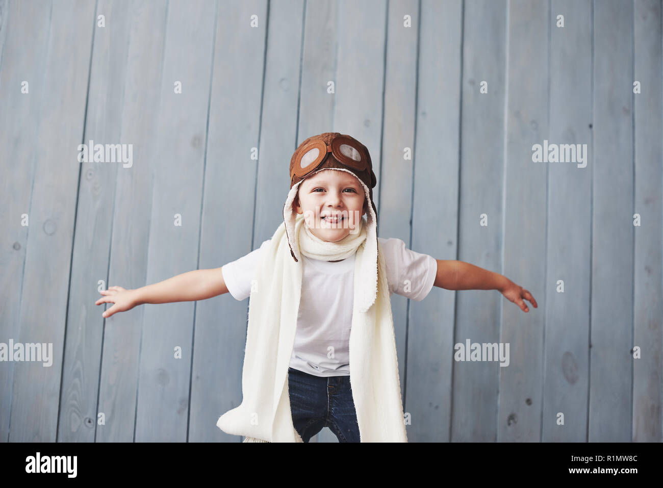 Beautiful smiling child in helmet on a blue background playing with a plane. Vintage pilot concept Stock Photo