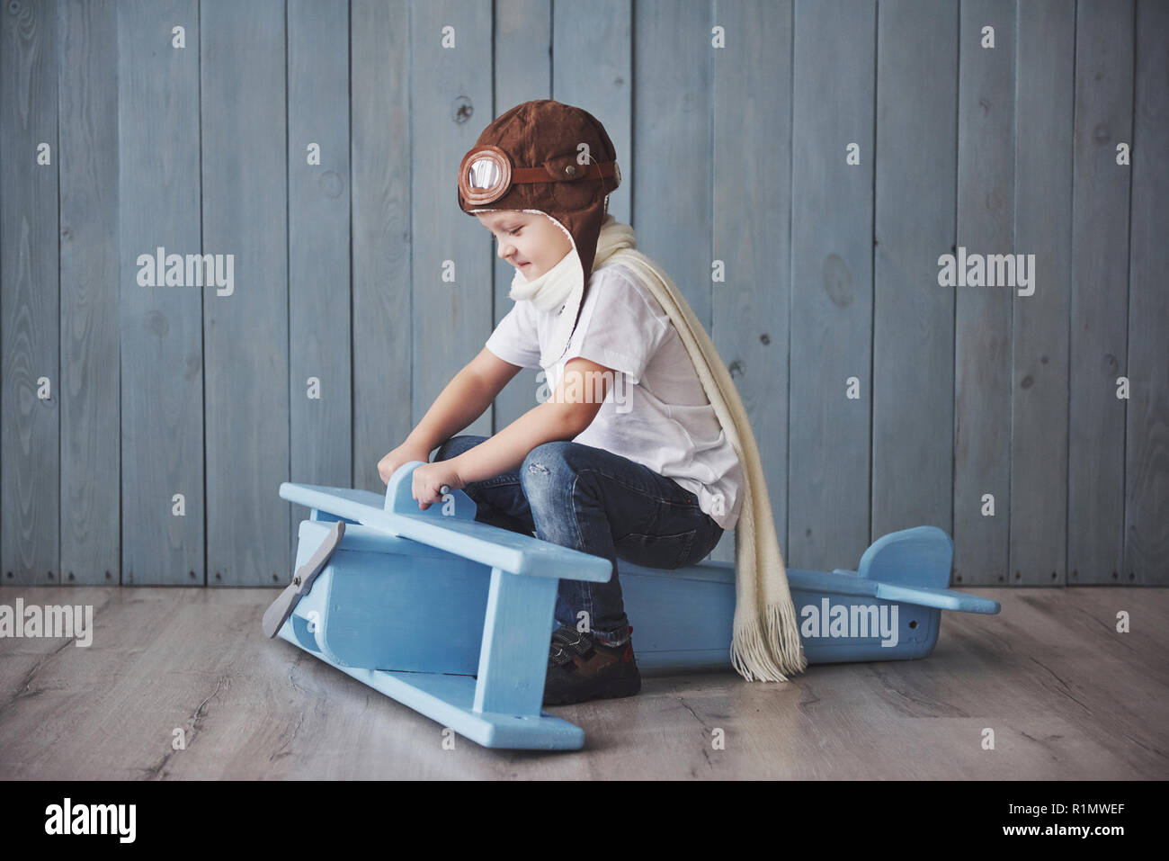 Happy kid in pilot hat playing with wooden airplane against. Childhood ...