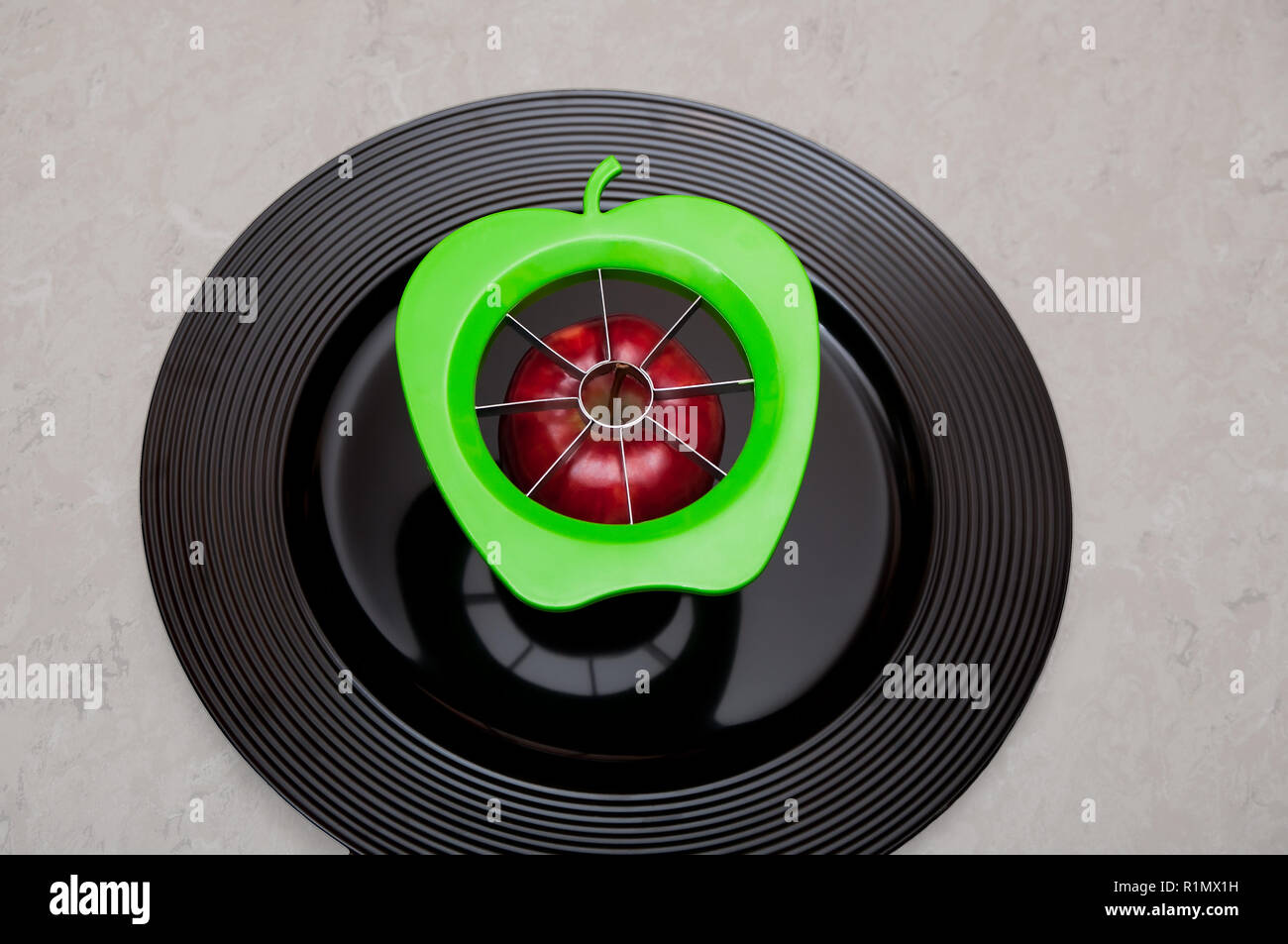 A green modern apple cutter with an organic, red healthy apple full of natural vitamins and nutrition on a plate ready to be cut to a fresh vegetarian raw snack dish Stock Photo