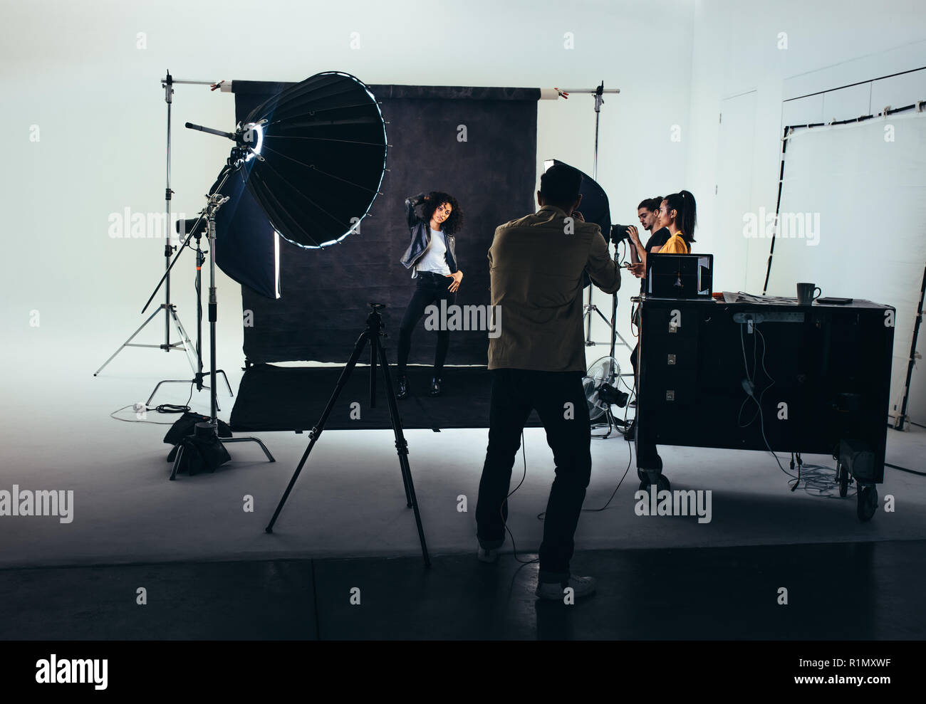 Photographer shooting photos of a female model with studio flash lights on. Photographer with his team during a photo shoot. Stock Photo