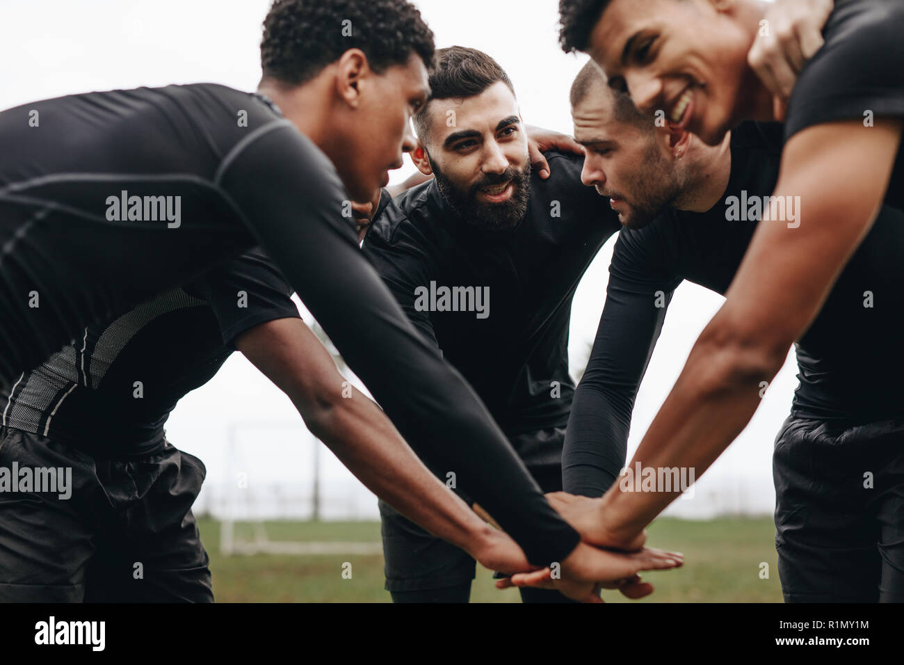 Soccer players joining hands in huddle talking about the game strategy. Low angle view of footballers bending forward in a huddle holding hands. Stock Photo