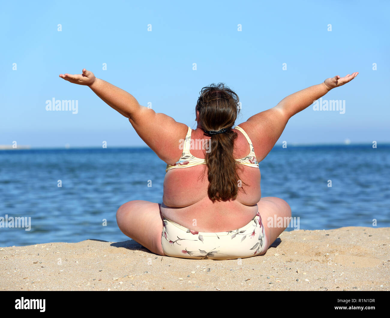 overweight woman on beach with hands up Stock Photo