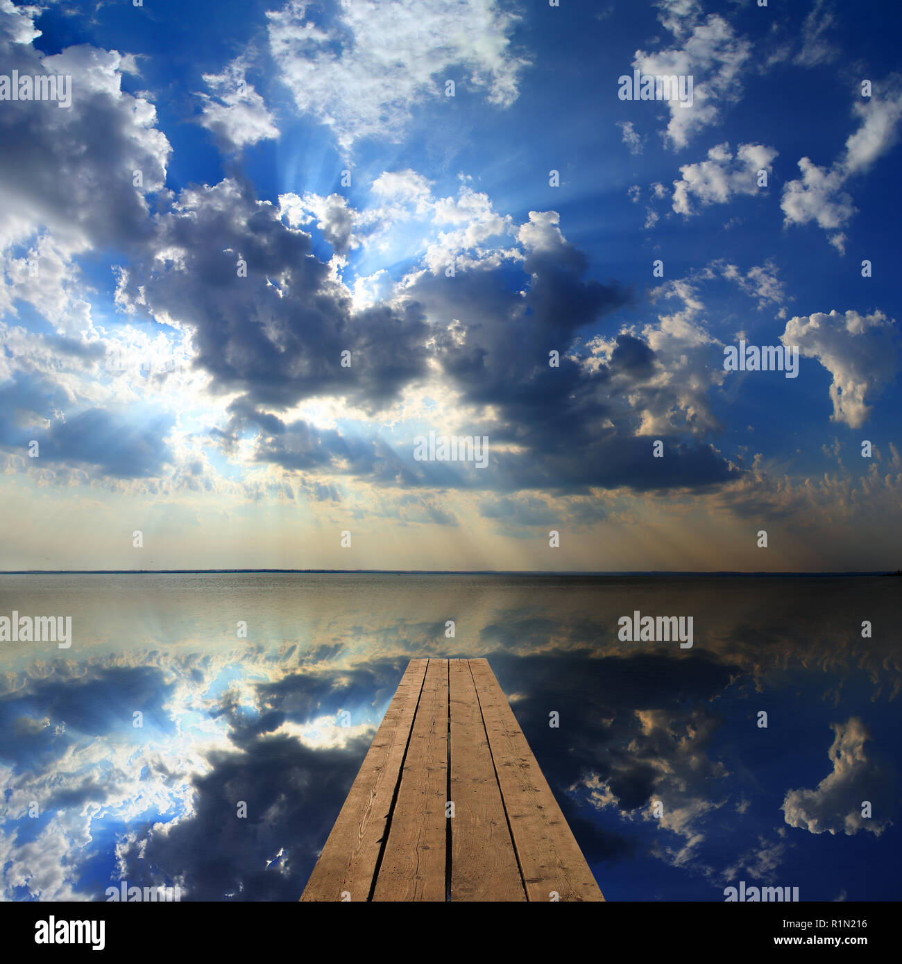 wooden pier on big lake and sky reflection Stock Photo