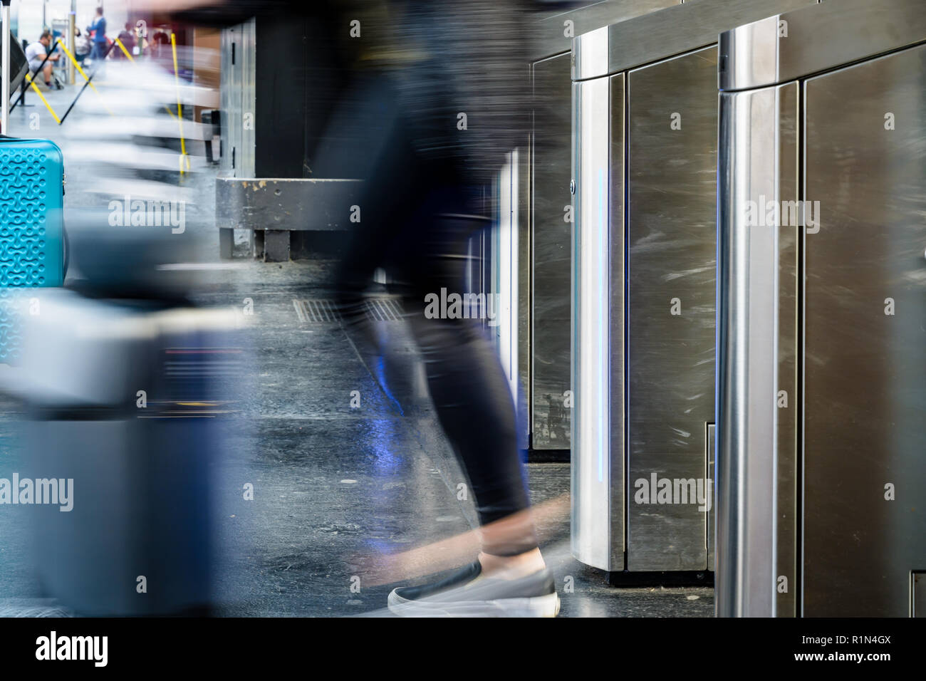 Side view of a woman with a rolling suitcase passing through stainless steel ticket gates in a public transportation station in Paris with motion blur Stock Photo