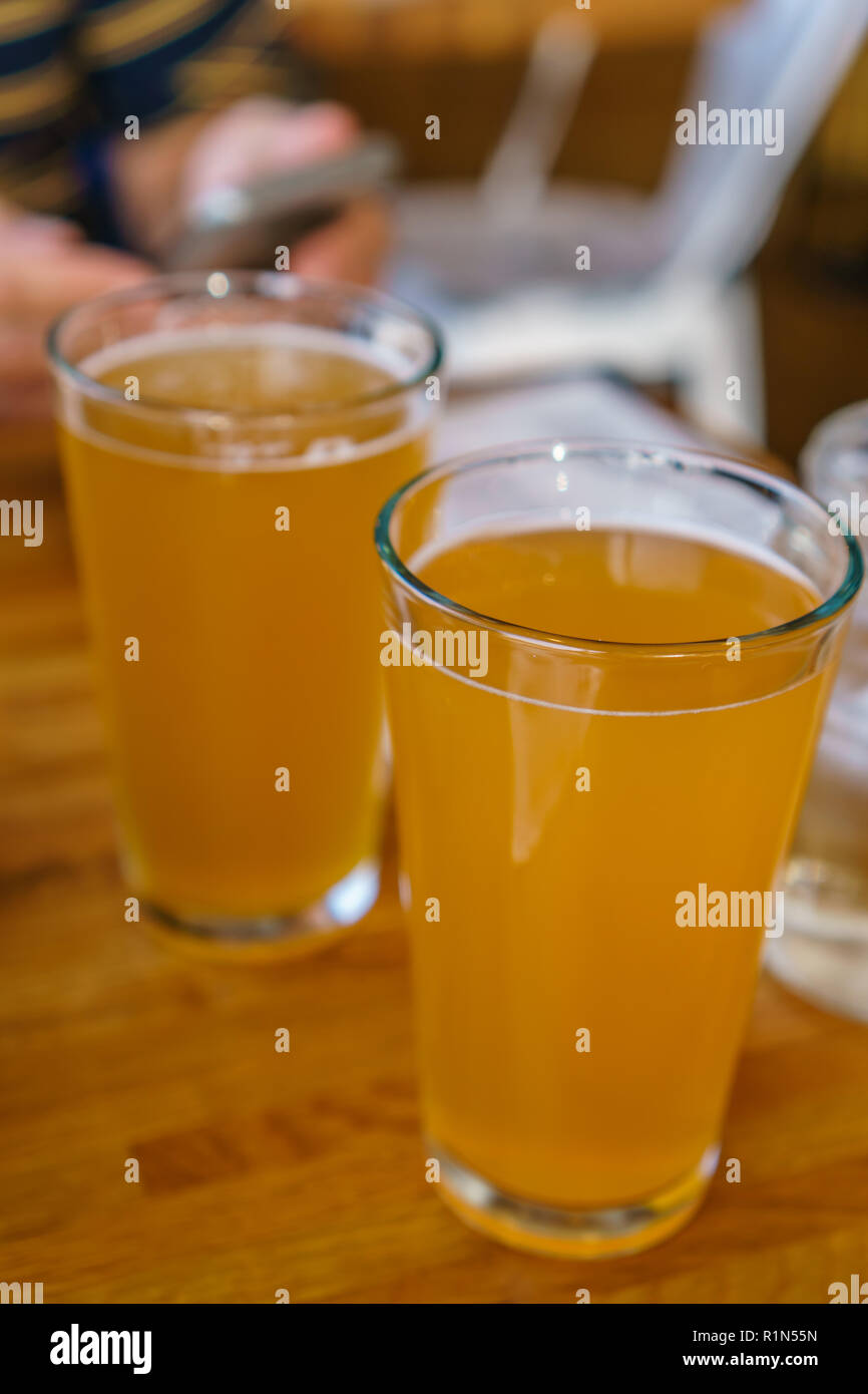 Close up of two tall glasses of beer on a table at a restaurant with person holding mobile phone in background Stock Photo