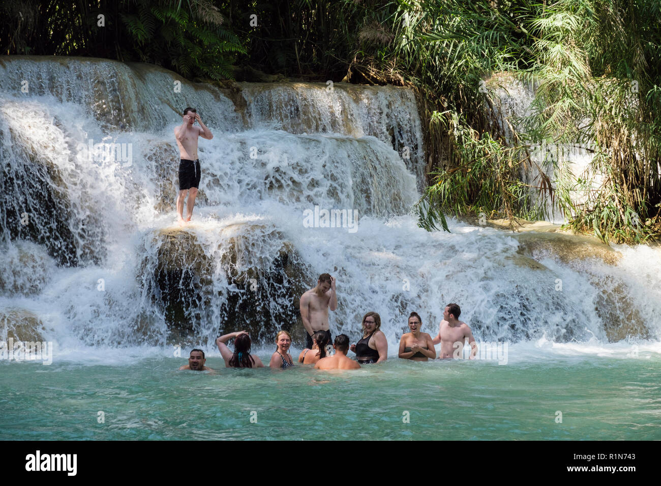 Young people having fun wild swimming in cool waters of a pool at Tat Kuang Si waterfalls with water cascading over rocks. Luang Prabang, Laos, Asia Stock Photo