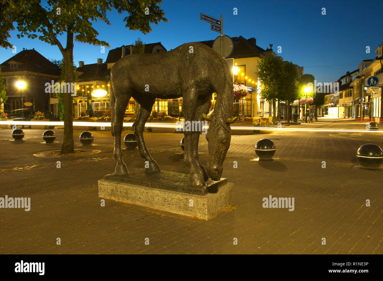 Sculpture of a horse by night in the center of the city of Baarn with a cafe and restaurant in the background with lights, the Netherlands Stock Photo