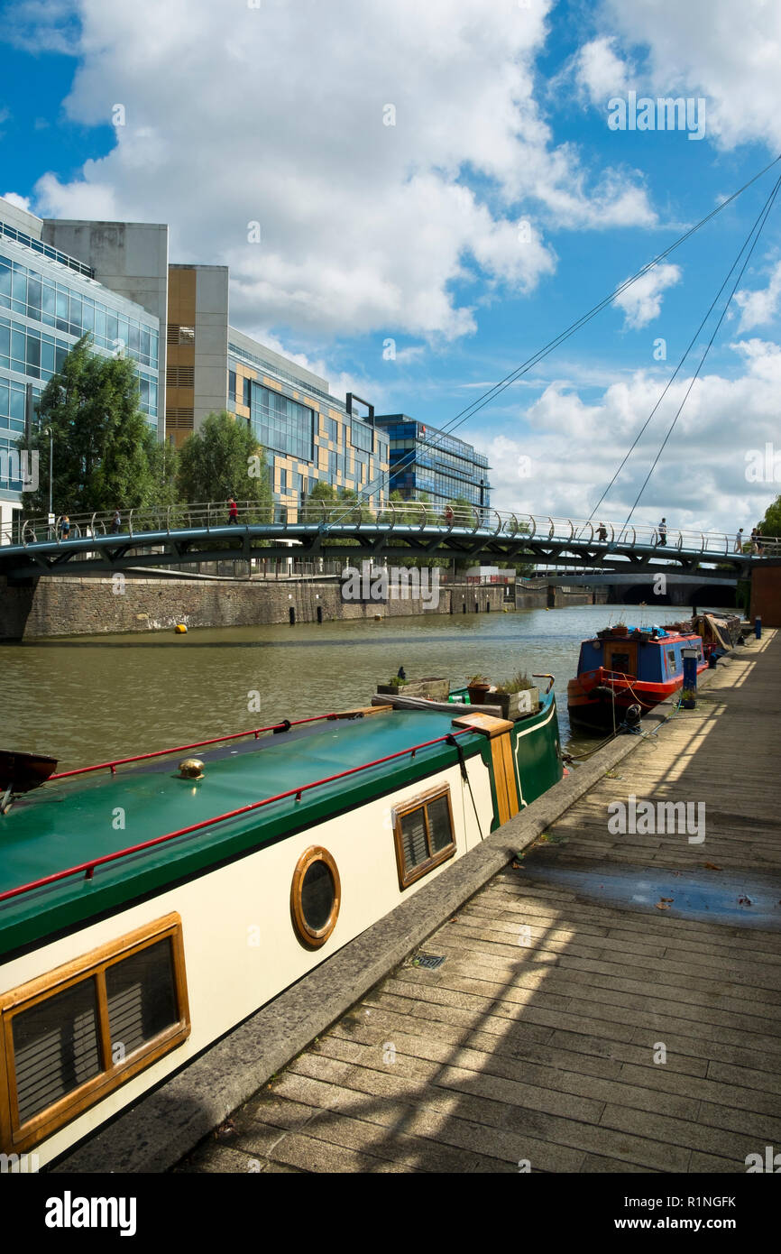 Bristol, UK - 4th August 2016: Moored canal boats and modern office blocks along The Floating Harbour and Temple Back (Temple Quay) regeneration business area in central Bristol City, UK. Workers cross Valentine Bridge during a sunny summertime lunch break. Stock Photo