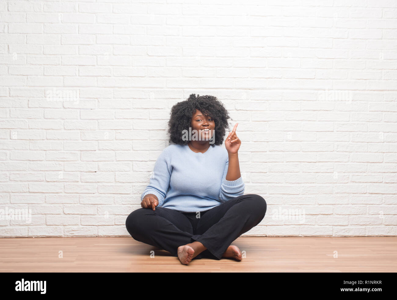 Young african american woman sitting on the floor at home pointing ...